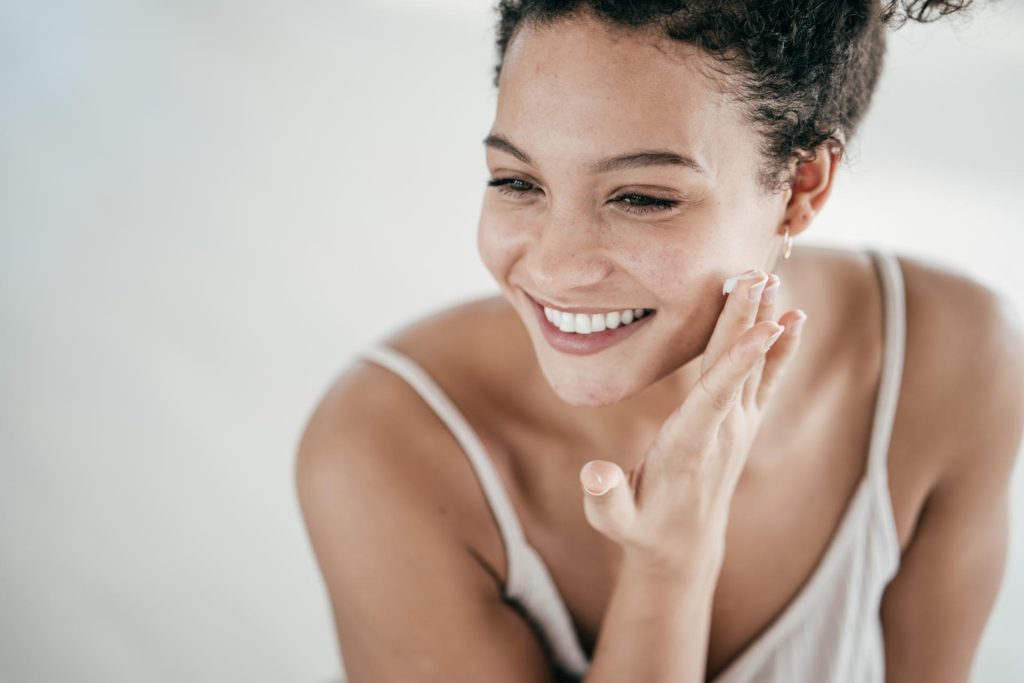 Smiling young women applying moisturizer to her face