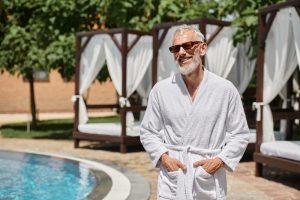 man standing outside in bathrobe at the pool wearing sunglasses